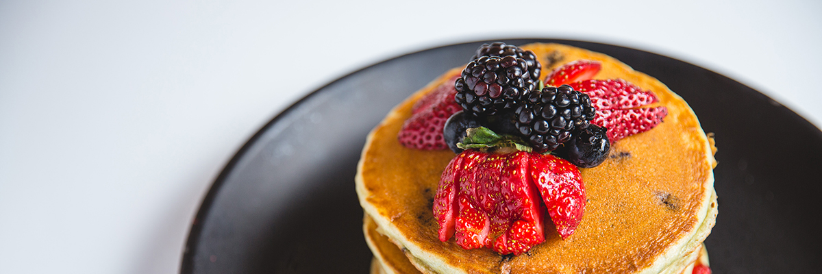 A stack of pancakes on a black plate, topped with fresh strawberries, blackberries and blueberries.