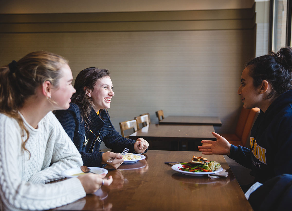 Three students sitting at a table eating and chatting.