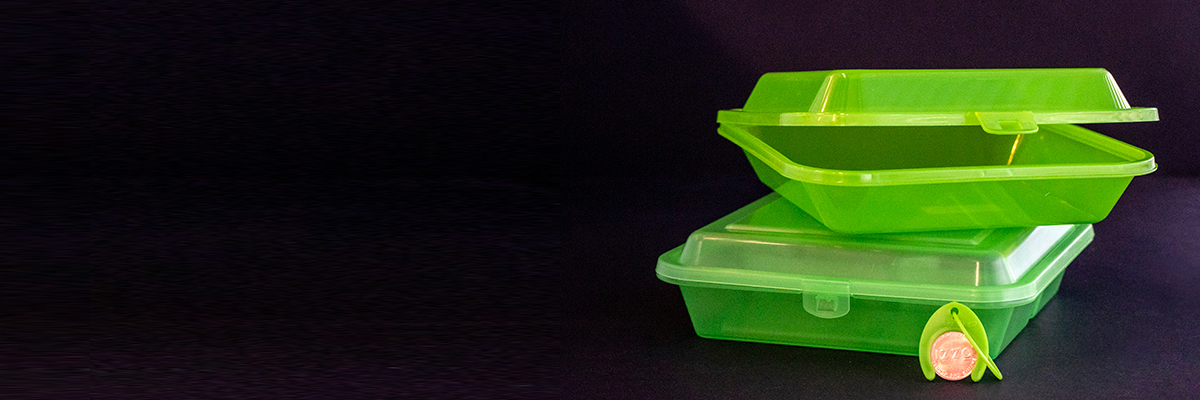 Green reusable to-go container and token on a black background.