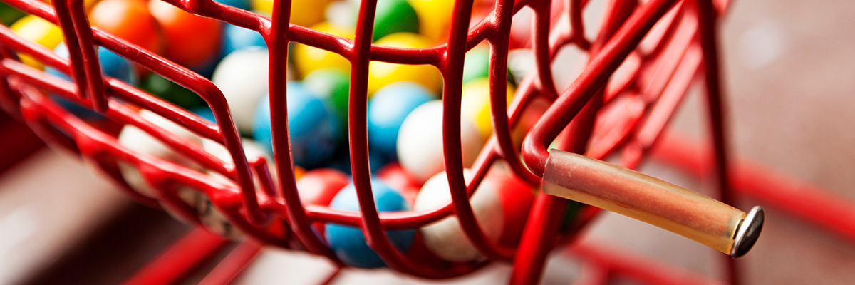 A close-up image of a red bingo wheel with multi-coloured bingo balls and a wooden handle.