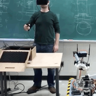 Animated gif of a robotic arm and a human operator. The Human is wearing a VR headset and using VR controllers to move the robotic arm in a synchronized way.